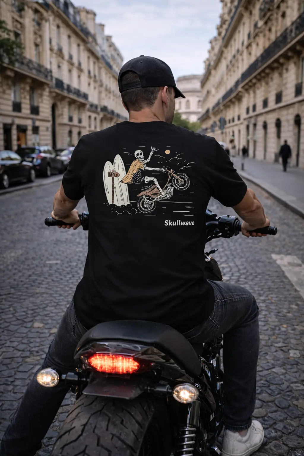 Homme portant un t-shirt noir Skull Rider avec illustration au dos en roulant en moto dans une rue urbaine