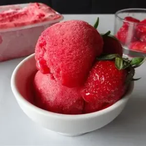 Boules de sorbet fraise artisanal dans une coupelle avec fraises fraîches en arrière-plan