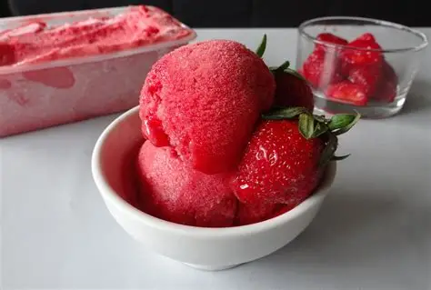 Boules de sorbet fraise artisanal dans une coupelle avec fraises fraîches en arrière-plan